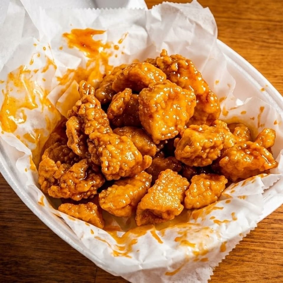 Crispy orange chicken pieces coated in sweet and sour sauce, served in a white takeout container.